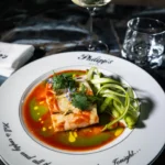 Colorful gourmet soup garnished with fresh herbs and vegetables, served on a white plate at Philipp's Club Milano