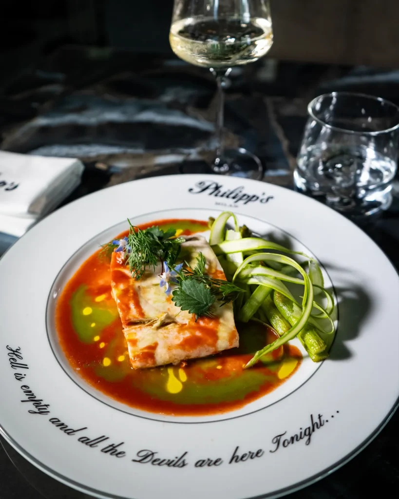 Colorful gourmet soup garnished with fresh herbs and vegetables, served on a white plate at Philipp's Club Milano