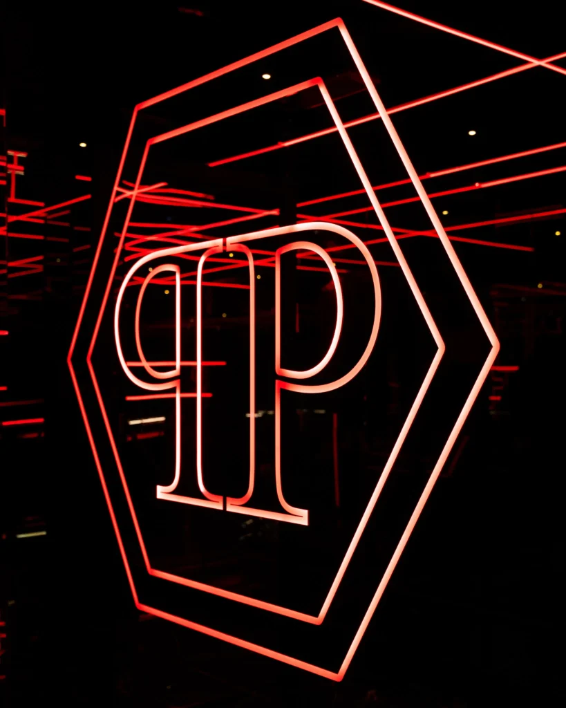 Red neon geometric emblem and stylized lettering on a dark wall at Philipp's Club Milano
