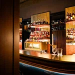 Sophisticated cocktail bar with illuminated bottle displays, dark wood finishes and warm ambient lighting at Portrait Milano