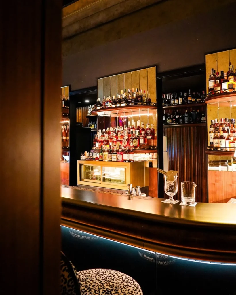 Sophisticated cocktail bar with illuminated bottle displays, dark wood finishes and warm ambient lighting at Portrait Milano