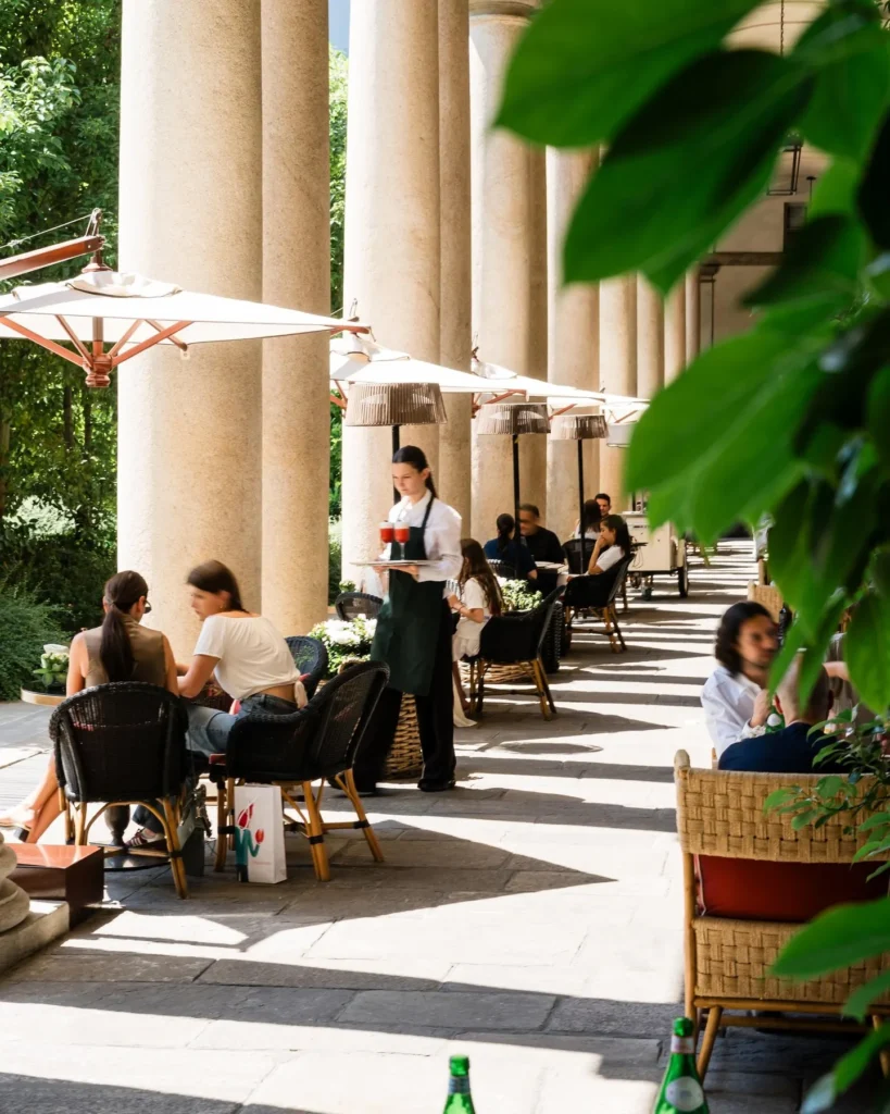 Outdoor restaurant seating beneath tall stone arches with potted greenery at Portrait Milano