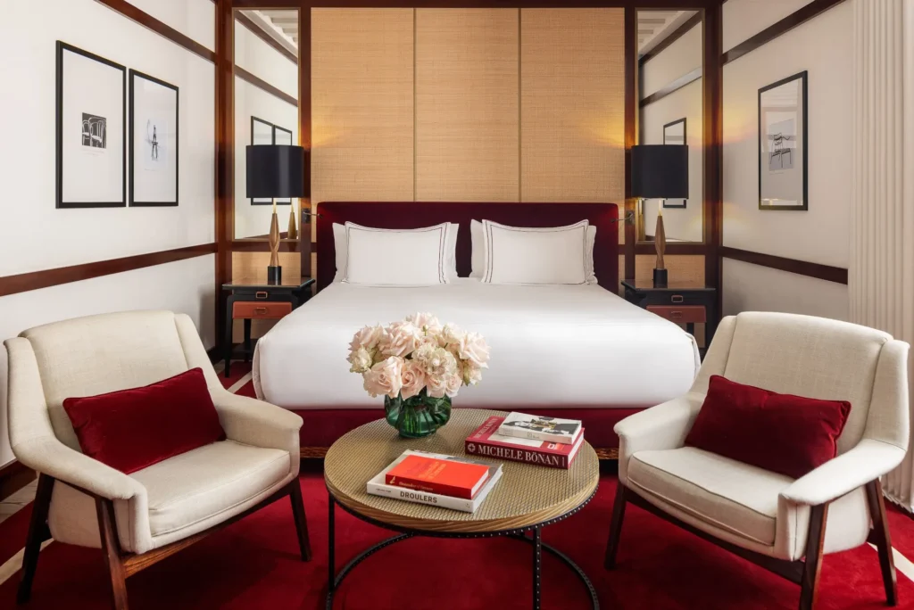 Elegant bedroom at Portrait Milano with a king-size bed, decorative wall panels, cream armchairs and a red carpet