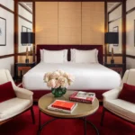 Elegant bedroom at Portrait Milano with a king-size bed, decorative wall panels, cream armchairs and a red carpet