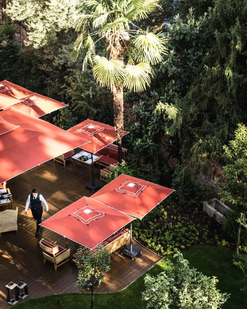 Elevated view of outdoor dining tables beneath red parasols surrounded by greenery at Portrait Milano