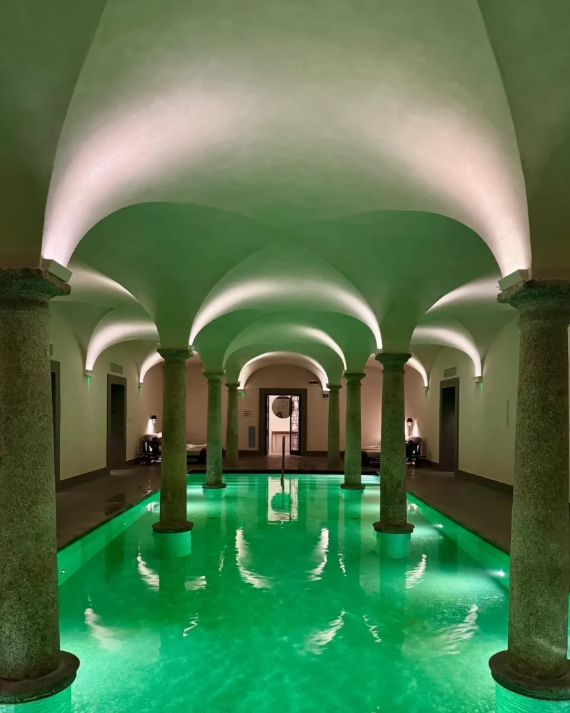 Serene spa pool beneath illuminated vaulted arches at Portrait Milano with turquoise water and classical architectural details