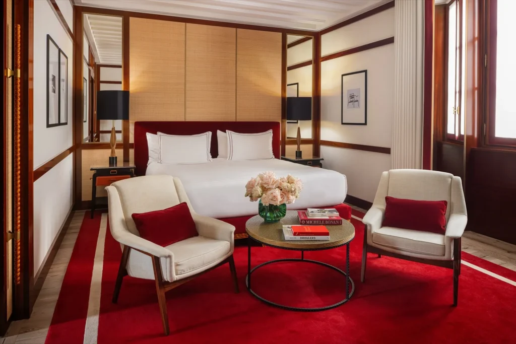Luxury studio suite bedroom with a king-size bed, red carpet, cream armchairs and refined contemporary furnishings at Portrait Milano