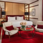Luxury studio suite bedroom with a king-size bed, red carpet, cream armchairs and refined contemporary furnishings at Portrait Milano