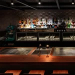 Atmospheric hotel bar with a backlit display of bottles and a dark elegant interior at Rosewood Hôtel de Crillon