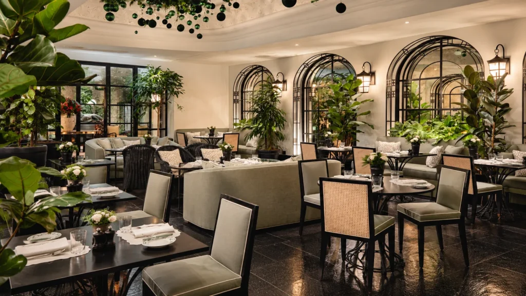 Refined dining lounge at The Carlton Milan with arched windows, leafy greenery, elegant tables, and upholstered chairs