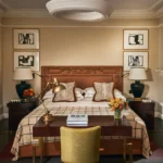Elegant bedroom at The Carlton Milan with a decorative headboard, layered bedding, framed artwork, and warm neutral furnishings