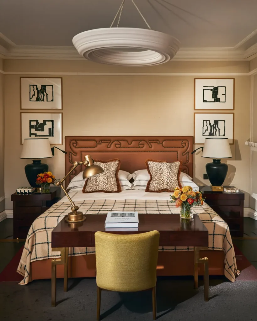 Elegant bedroom at The Carlton Milan with a decorative headboard, layered bedding, framed artwork, and warm neutral furnishings