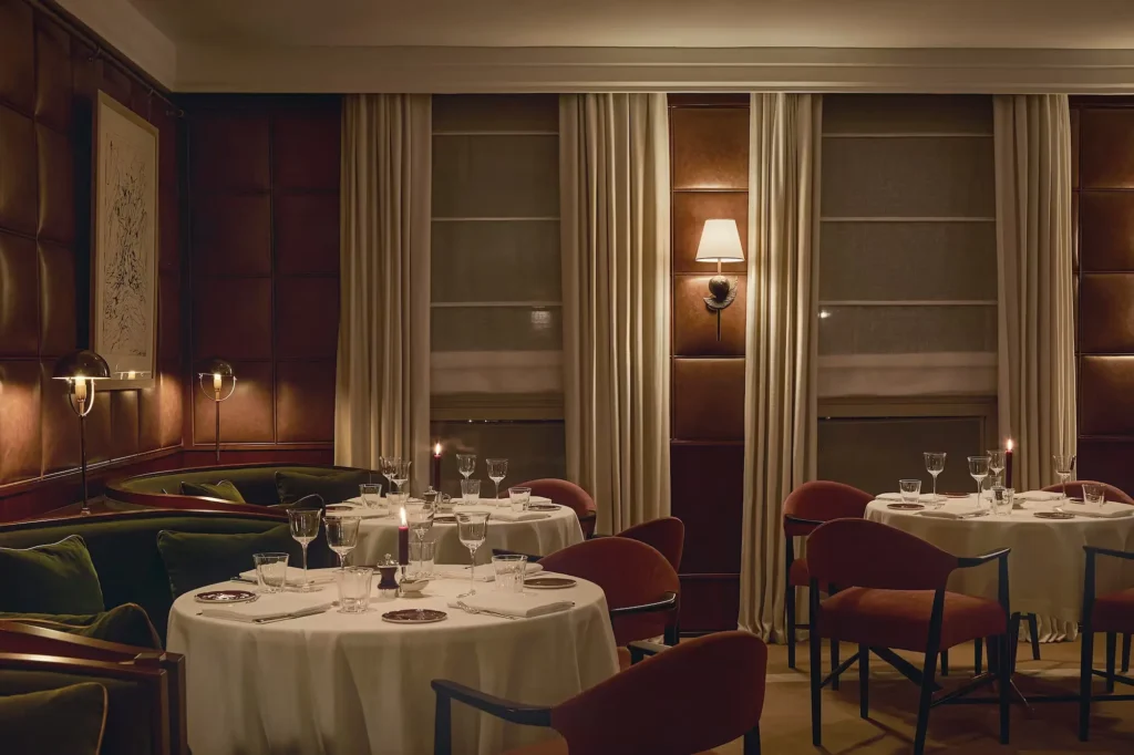 Sophisticated fine dining room at The Carlton Milan with round white-tablecloth tables, burgundy chairs, and warm ambient lighting