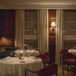 Sophisticated fine dining room at The Carlton Milan with round white-tablecloth tables, burgundy chairs, and warm ambient lighting