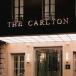 The Carlton Milan hotel sign above the entrance, set against a dark facade and elegant stone exterior