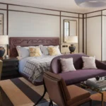 Luxury guest bedroom at The Carlton Milan featuring a plush bed, muted pink and cream tones, elegant artwork, and a comfortable armchair