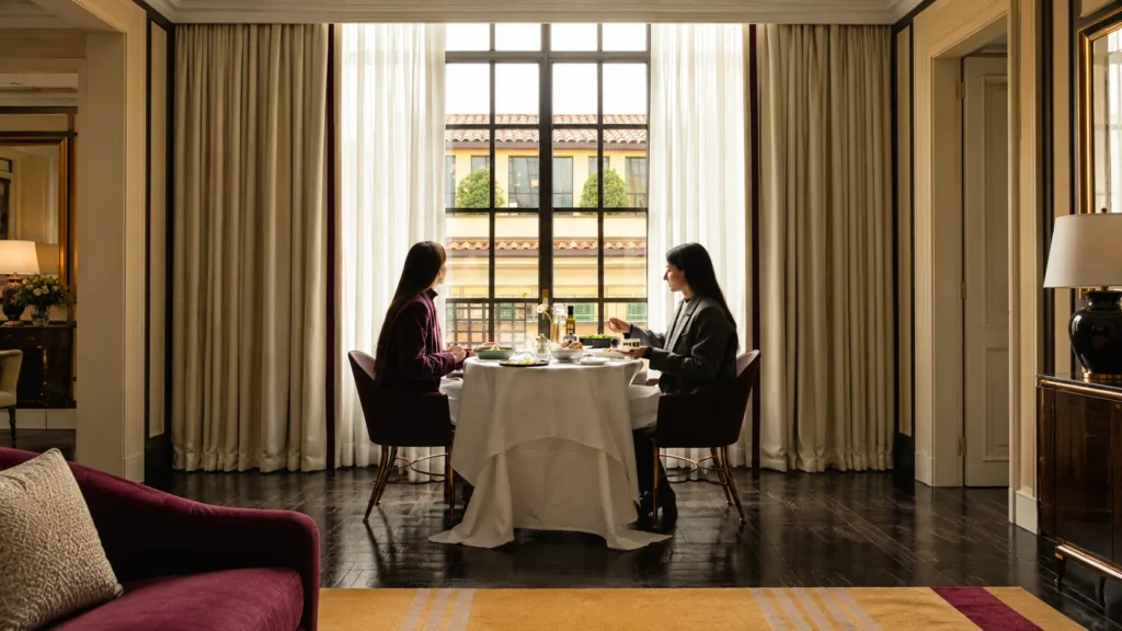 Elegant restaurant table beside a large sunlit window at The Carlton Milan, surrounded by curtains and sophisticated furnishings