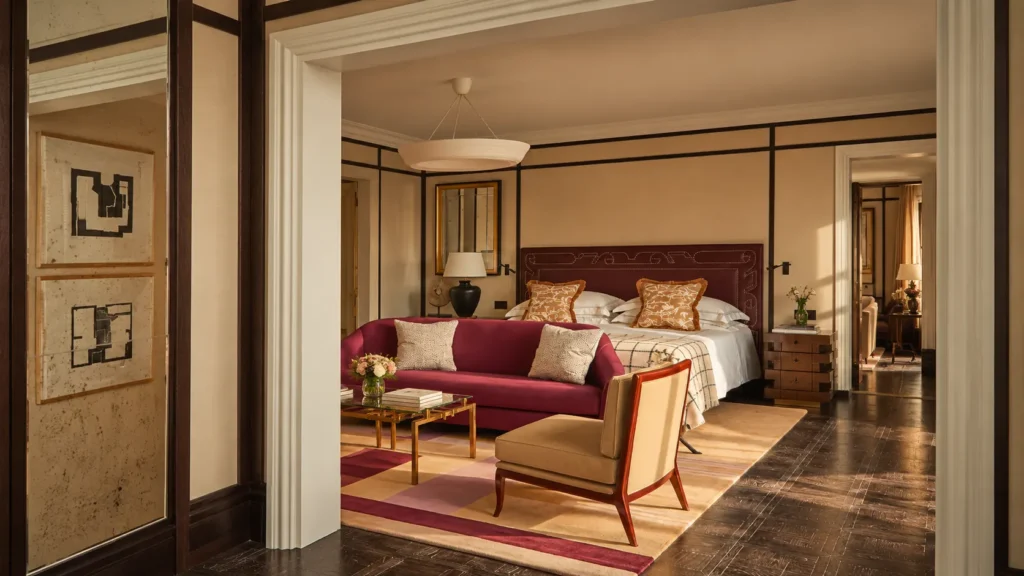 Warm luxury suite interior at The Carlton Milan featuring a king-size bed, burgundy sofa, patterned rug, and elegant contemporary furnishings